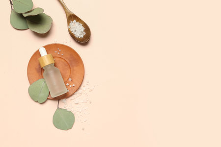 Bottle of cosmetic oil with sea salt and eucalyptus branch on beige backgroundの写真素材