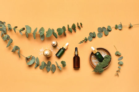 Wooden plate with bottles of cosmetic oil and eucalyptus branch on orange backgroundの写真素材