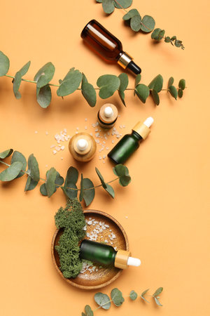Wooden plate with bottles of cosmetic oil and eucalyptus branch on orange backgroundの写真素材