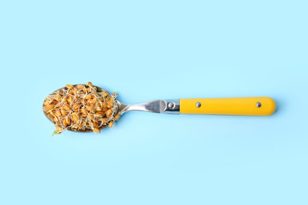Spoon with sprouted wheat on light blue background