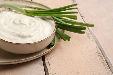 Bowl of tasty sour cream with green onion on light wooden backgroundの写真素材