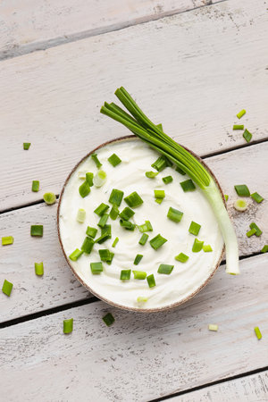 Bowl of tasty sour cream with green onion on light wooden backgroundの写真素材