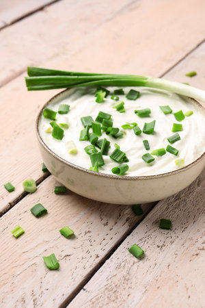 Bowl of tasty sour cream with green onion on light wooden backgroundの写真素材