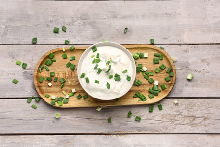 Bowl of tasty sour cream with green onion on light wooden backgroundの写真素材