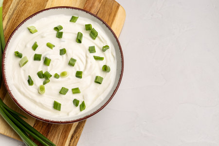 Bowl of tasty sour cream with green onion on light backgroundの写真素材