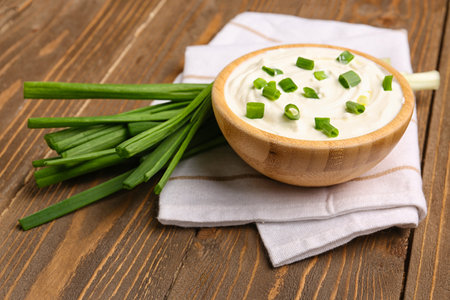 Bowl of tasty sour cream with green onion on wooden backgroundの写真素材