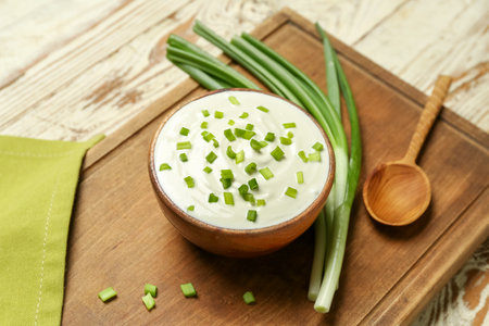 Bowl of tasty sour cream with green onion on light wooden backgroundの写真素材