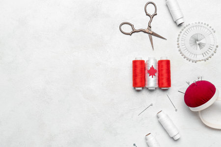 Thread spools with maple leaf, pin cushion and scissors on white background. Canadian flag concept