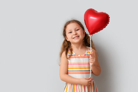 Little girl with heart shaped balloon on light background. Children's Day celebrationの写真素材