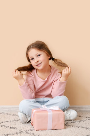 Little girl with gift sitting near beige wall. Children's Day celebrationの写真素材