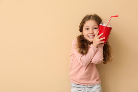 Little girl with cup of soda on beige background. Children's Day celebrationの写真素材