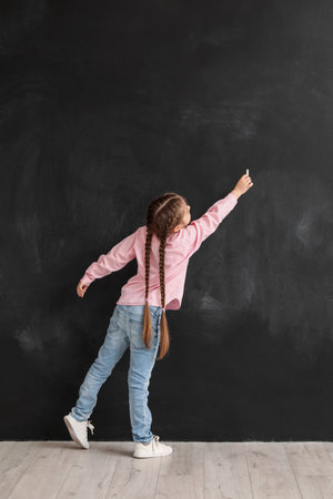 Little girl drawing with chalk piece on blackboard, back view. Children's Day celebrationの写真素材