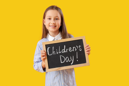 Little girl holding chalkboard with text CHILDREN'S DAY on yellow backgroundの写真素材