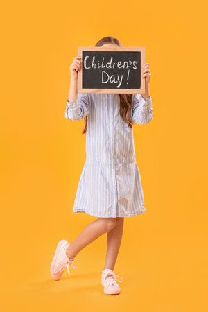 Little girl holding chalkboard with text CHILDREN'S DAY on yellow backgroundの写真素材