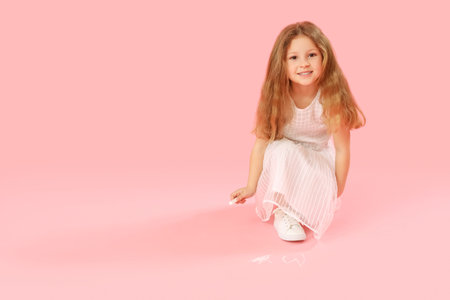 Little girl drawing with chalk piece on pink background. Children's Day celebrationの写真素材