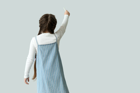 Little girl with chalk piece on light background, back view. Children's Day celebrationの写真素材