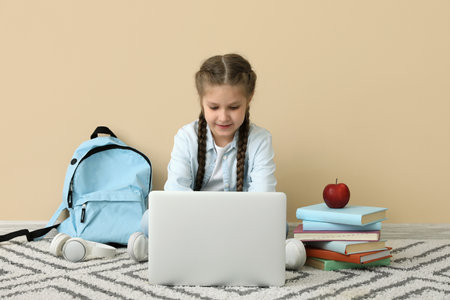 Little girl studying with laptop near beige wall. Children's Day celebrationの写真素材