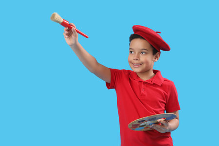 Little African-American artist with brush and paint palette on blue background. Children's Day celebrationの写真素材