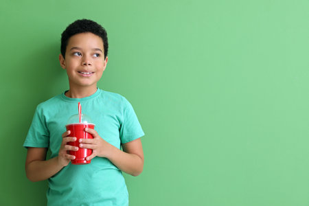 Little African-American boy with cup of soda on green background. Children's Day celebrationの写真素材