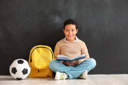 Little African-American boy reading book near blackboard. Children's Day celebrationの写真素材