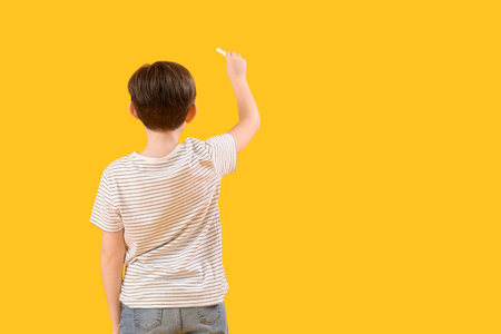 Little boy drawing with chalk piece on yellow background, back view. Children's Day celebrationの写真素材
