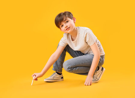 Little boy drawing with chalk piece on yellow background. Children's Day celebrationの写真素材
