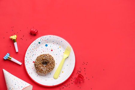 Paper disposable plate with donut, party blowers and hat on red backgroundの写真素材