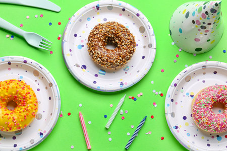 Paper disposable tableware with donuts, party hat and candles on green backgroundの写真素材