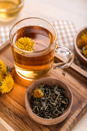 Board with bowl and glass cup of healthy dandelion tea on white wooden backgroundの写真素材
