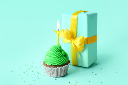 Tasty cupcake with birthday candle and gift box on blue backgroundの写真素材