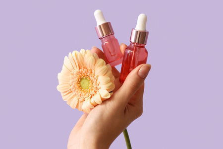 Hand holding bottles of essential oil and flower on lilac backgroundの写真素材