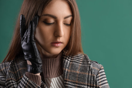 Beautiful young woman in leather gloves and coat on green backgroundの写真素材