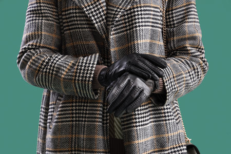 Beautiful woman in leather gloves and coat on green background, closeup