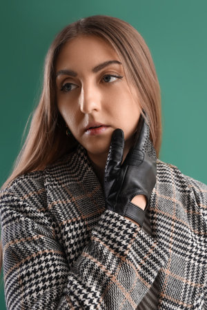 Portrait of beautiful young woman in leather gloves and coat on green backgroundの写真素材