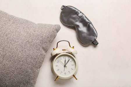 Sleeping mask with alarm clock and pillow on light backgroundの写真素材