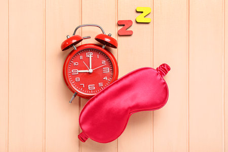 Sleep mask and alarm clock with text ZZZ on pink wooden backgroundの写真素材