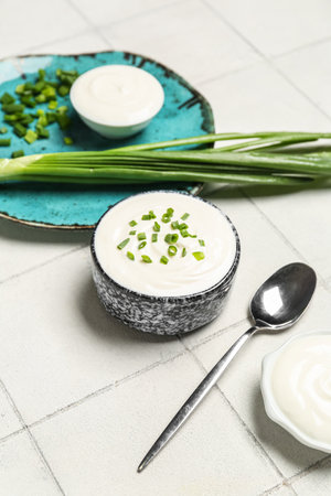 Bowl of tasty sour cream with green onion on white tile backgroundの写真素材