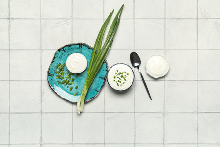 Bowls of tasty sour cream with green onion on white tile backgroundの写真素材