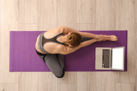 Sporty young woman with laptop doing yoga in gym, top viewの写真素材