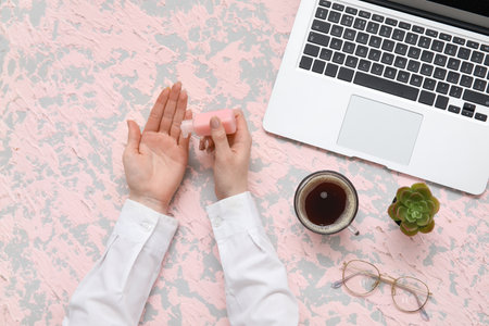 Woman applying hand sanitizer at table in officeの写真素材