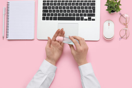 Woman applying hand sanitizer at pink table in officeの写真素材