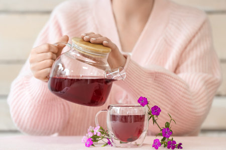 Woman pouring hot tea from teapot into cup with delicate flowers on tableの写真素材