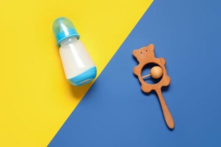 Bottle of milk for baby and rattle on color backgroundの写真素材