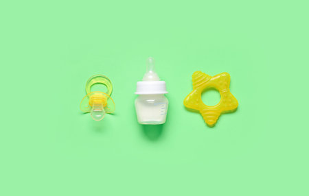 Bottle of milk for baby and accessories on pale green background