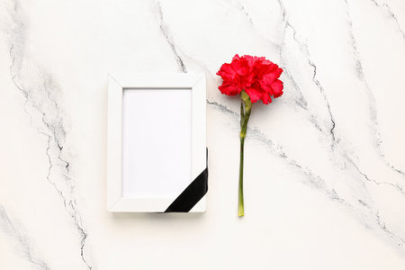 Photo frame with black ribbon and red carnation on white grunge backgroundの写真素材