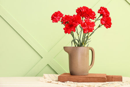 Vase with red carnations on white wooden table near light green wallの写真素材