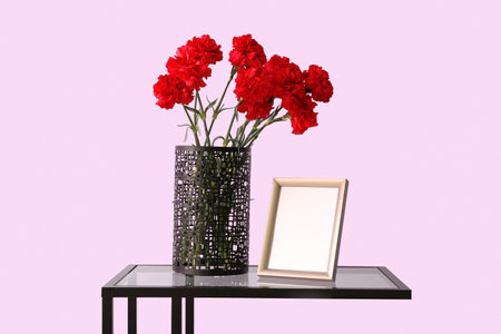 Vase with red carnations and photo frame on table near lilac wallの写真素材
