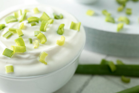 Bowl with sour cream and sliced green onion on white tile tableの写真素材