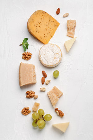 Different types of tasty cheese, nuts and grapes on light backgroundの写真素材