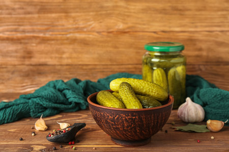 Jar and bowl with tasty canned cucumbers on wooden tableの写真素材